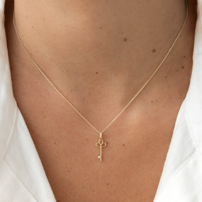 Key-shaped pendant necklace with a delicate chain, worn centered on the chest over a white top.
