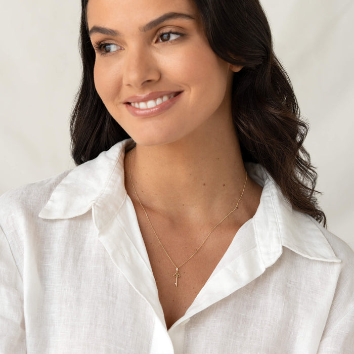 Model wearing a delicate Yellow Gold necklace with a small Key-shaped pendant, styled with a white collared shirt.