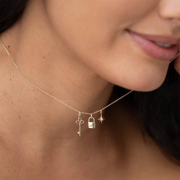 Close-up of a model wearing a delicate Yellow Gold necklace with three dangling charms: a key, a padlock, and a starburst charm.