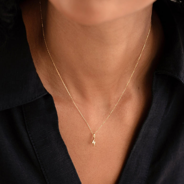 Close-up of a woman wearing a Diamond Lightning Bolt Charm 14k Gold pendant on a delicate gold chain with a black top