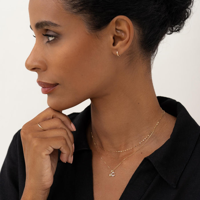 Close-up of woman wearing Diamond Star Charm 14k Gold necklace layered with delicate gold chains on black top