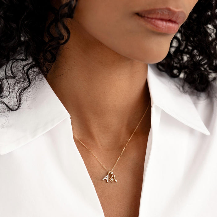 Close-up of a woman wearing a Diamond Star Charm 14k Gold necklace with two letter pendants on a white shirt