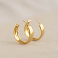 Close-up of Large Bold Hoop Earrings - Mina in gold vermeil with a wide rounded hoop design on a neutral background