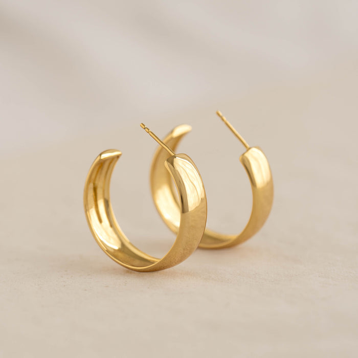Close-up of Large Bold Hoop Earrings - Mina in gold vermeil with a wide rounded hoop design on a neutral background