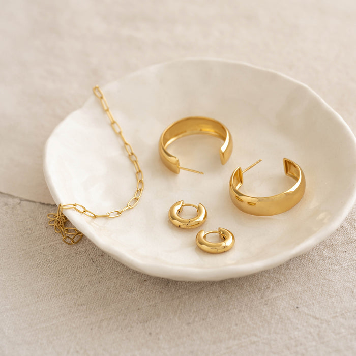 Close-up of Large Bold Hoop Earrings - Mina in gold vermeil displayed on a white ceramic dish with a gold chain necklace