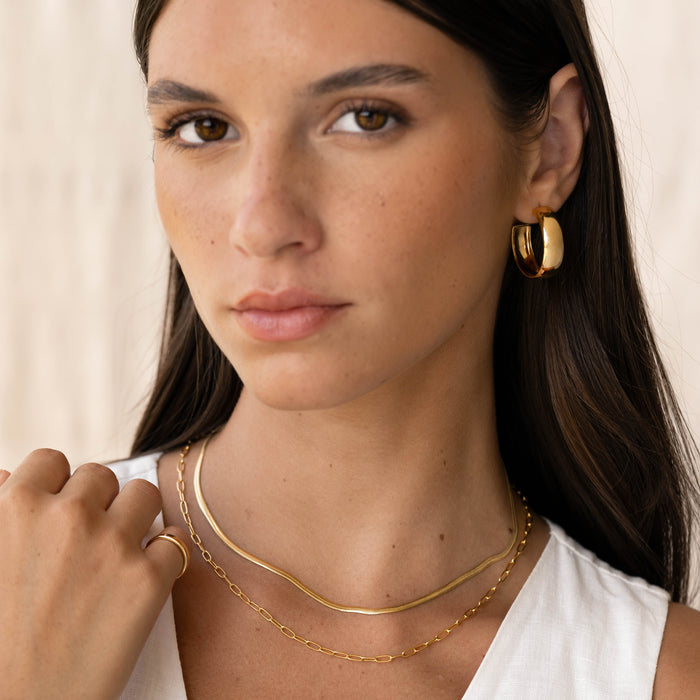 Close-up of a woman wearing Large Bold Hoop Earrings - Mina in gold vermeil with layered gold necklaces and white top