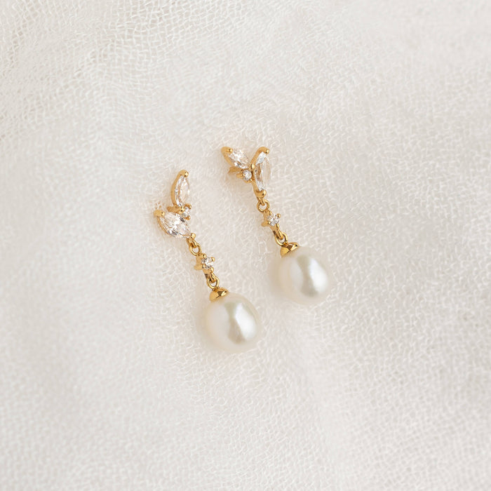 Elegant gold earrings with pearl and crystal accents rest on delicate white lace, exuding a sense of sophistication and classic beauty.