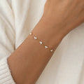 A delicate Gold bracelet with small white gemstones is elegantly worn on a wrist, framed by soft beige fabric, conveying a refined and minimalist style.