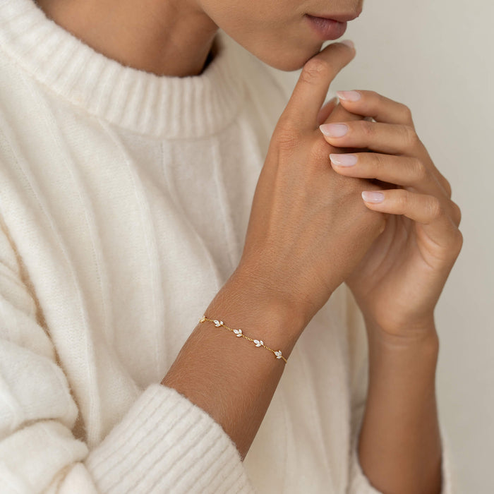 Close-up of a person in a white sweater with a delicate Gold bracelet featuring small floral designs. Their hands are gently clasped near their face, conveying a serene mood.