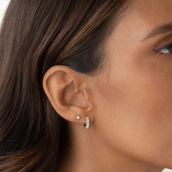 Close-up of a woman wearing March Birthstone Huggie Earrings - Blue Topaz in gold vermeil on her left ear