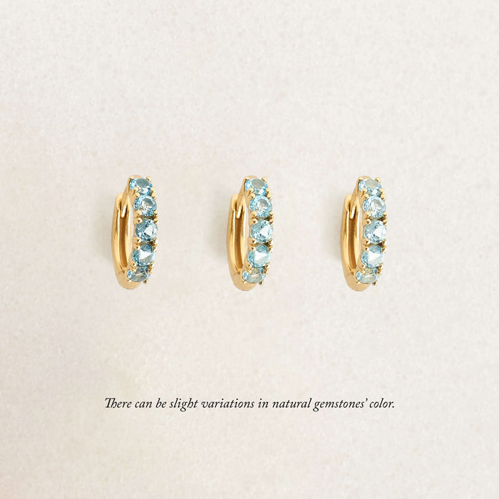 Three Gold Eternity huggie earrings featuring rows of small gemstones, displayed against a soft cream background.