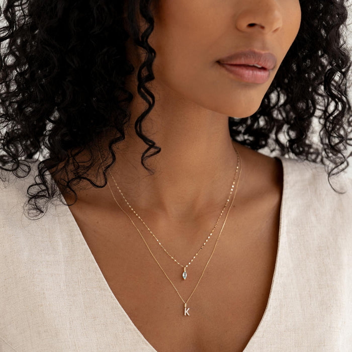 Close-up of a woman wearing the March Birthstone Pendant 14k Gold - Swiss Blue Topaz layered with a delicate gold initial necklace