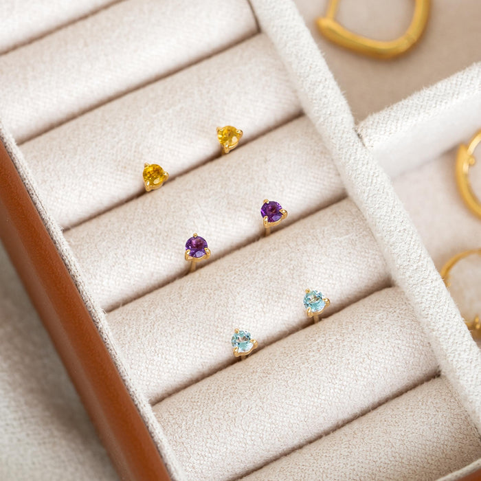 March Birthstone Stud Earrings 14k Gold - Blue Topaz pair with other gemstone studs displayed in a jewelry case