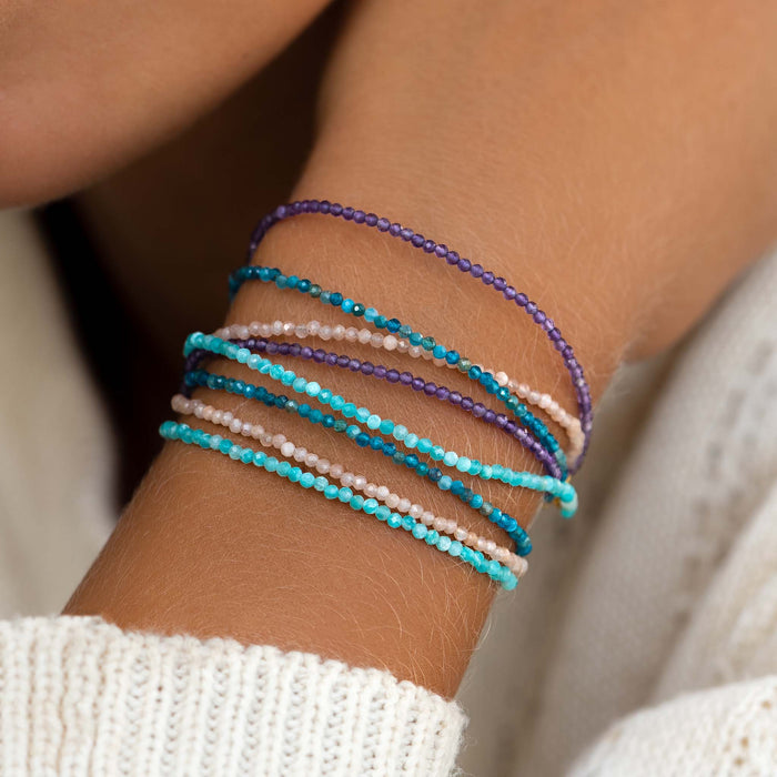 Close-up of a wrist wearing a Multi Strand Beaded Bracelet with purple, blue, and neutral small crystal beads