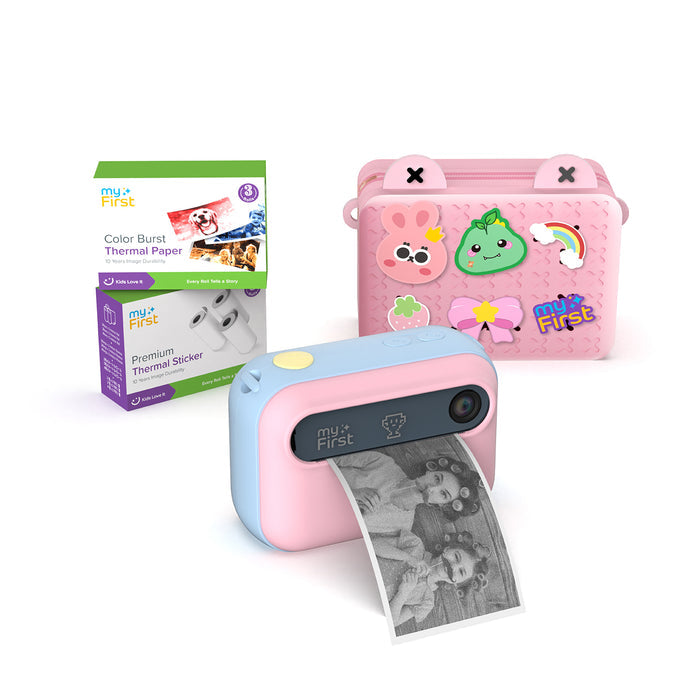 myFirst Insta 20 pink and blue instant print camera for kids printing a photo, shown with a carrying bag, Color Burst thermal paper, and sticker rolls.