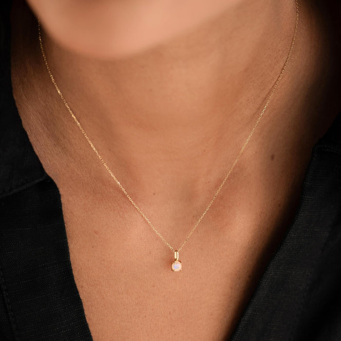 Close-up of a woman wearing the Opal Charm 14k Gold pendant on a delicate gold chain with a black top background