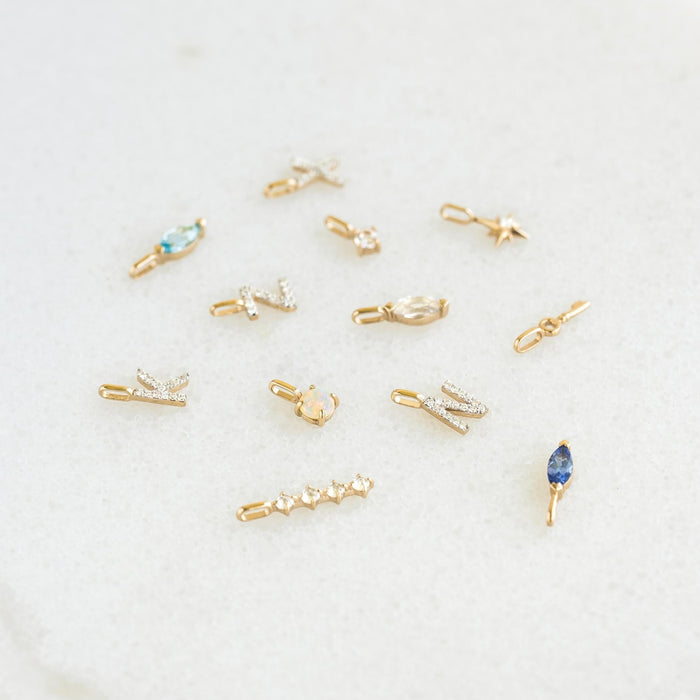 Assorted delicate 14k gold charms including opal and gemstone accents arranged on a light surface with Opal Charm 14k Gold displayed