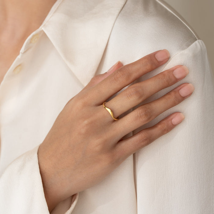 Close-up of a hand wearing the Organic Wavy Ring - Bea in gold vermeil over a cream blouse sleeve
