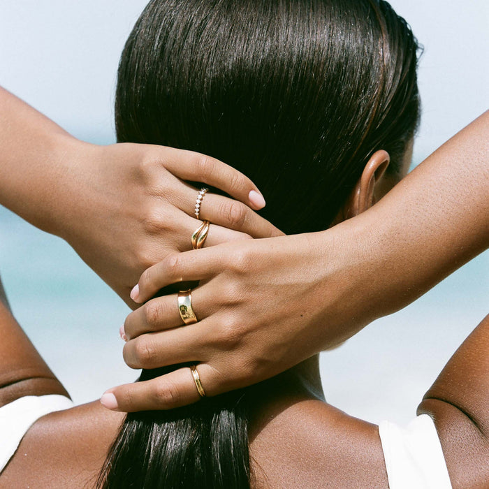Close-up of a woman’s hands behind her head wearing the Organic Wavy Ring - Bea in gold vermeil with other gold rings outdoors