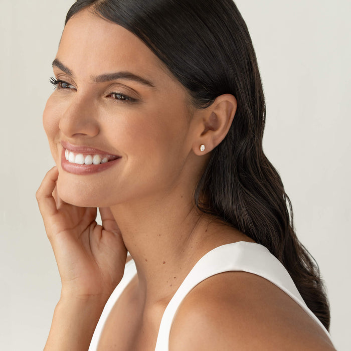 Smiling woman with dark hair wearing a small oval-cut gemstone stud earring set in Gold Vermeil, shown in a soft, natural portrait against a neutral background.