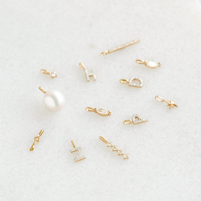 Pearl Charm 14k Gold rice pearl pendant charm among small 14k gold letter and star charms on white background