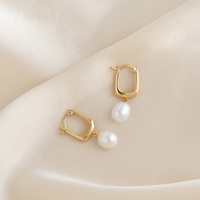 Close-up of Pearl Drop Hoop Earrings - Maeve in gold vermeil with freshwater pearl drops on a cream fabric background