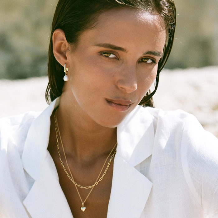 Woman wearing Pearl Drop Hoop Earrings - Maeve with layered gold necklaces and white linen shirt outdoors in natural light