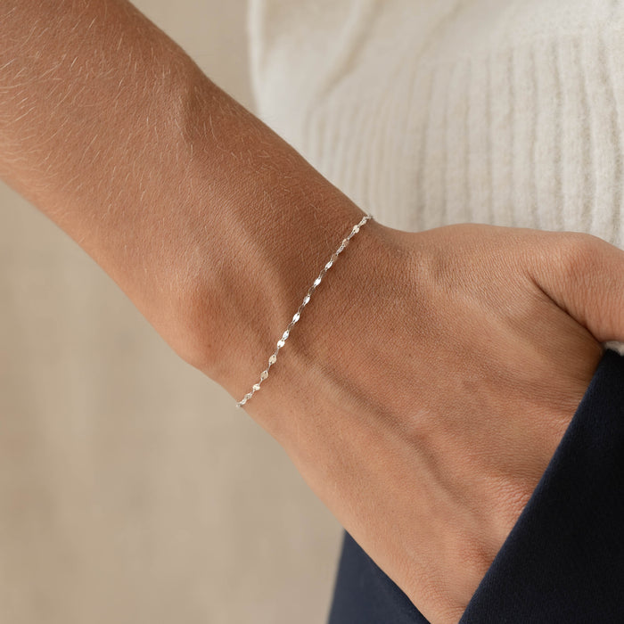 Close-up of a wrist wearing the Petal Chain Bracelet White Gold - Florence with a textured white top and navy pants