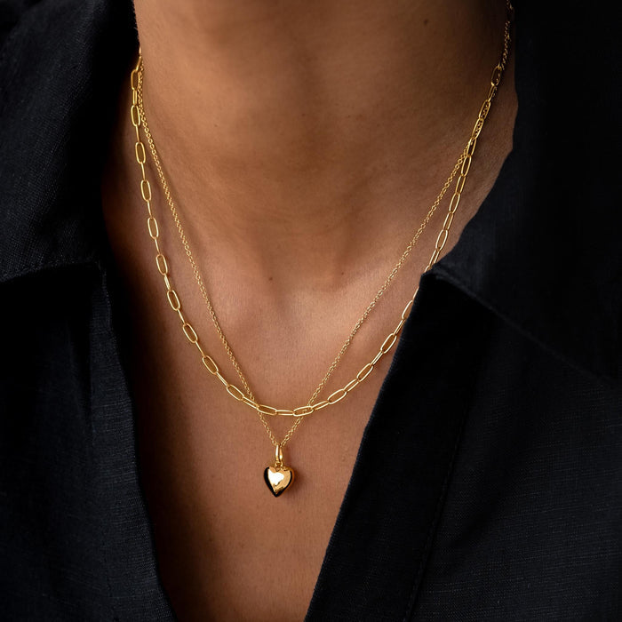 Gold heart pendant necklace stacked with paperclip chain on model