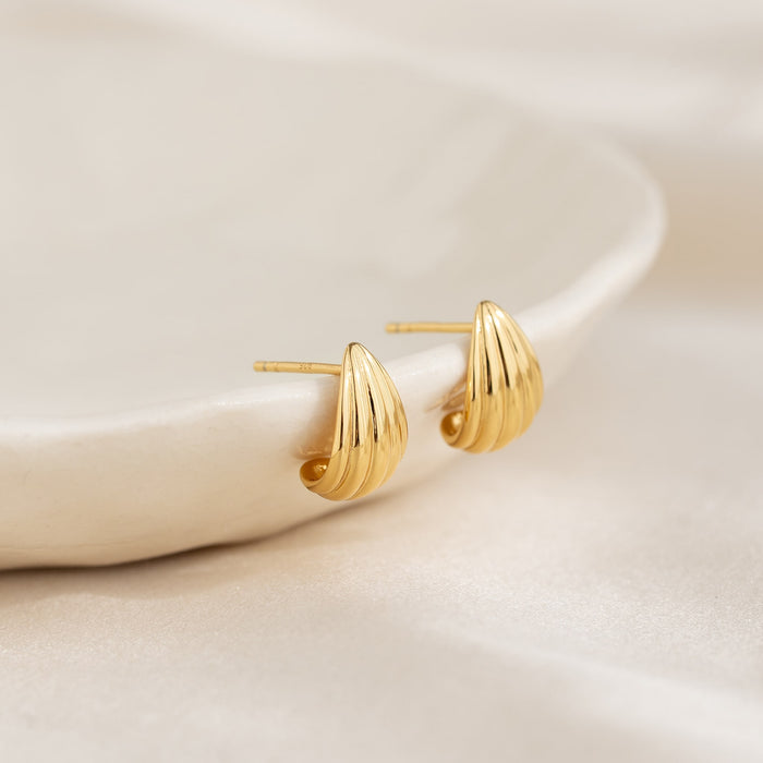 Close-up of Scalloped Huggie Earrings - Tulisa in gold vermeil resting on a smooth cream ceramic dish