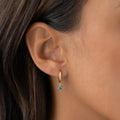 Close-up of a woman wearing September Birthstone Drop Huggie Earrings - London Blue Topaz with gold vermeil setting