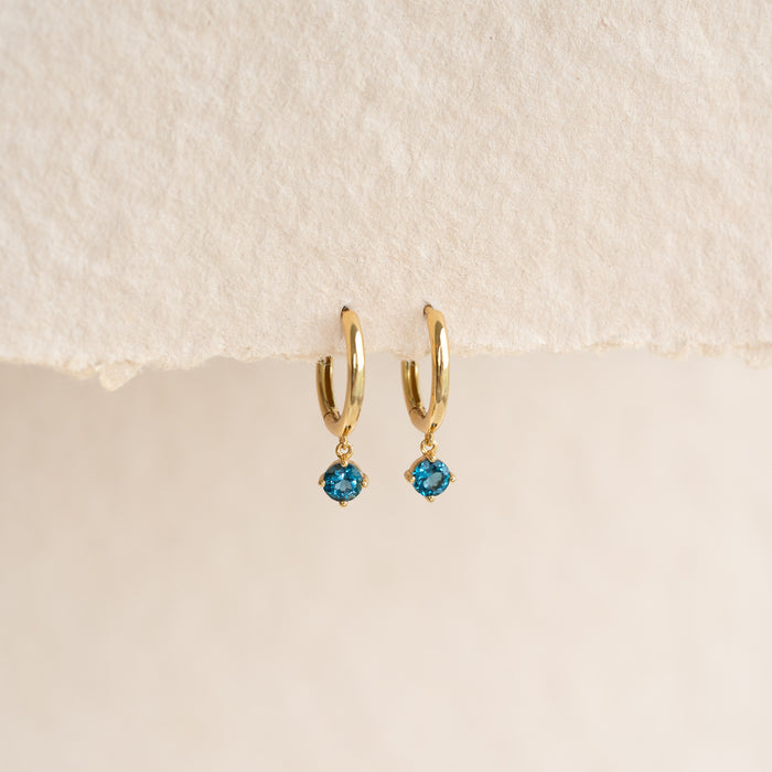 September Birthstone Drop Huggie Earrings - London Blue Topaz with gold vermeil setting on a neutral background