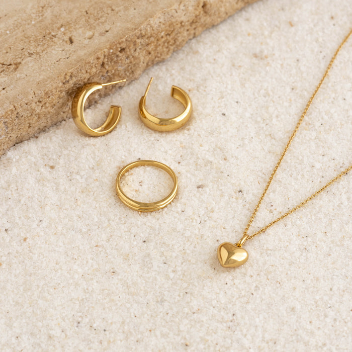 Small Bold Hoop Earrings - Ebba displayed alongside gold ring and heart pendant necklace on light textured surface