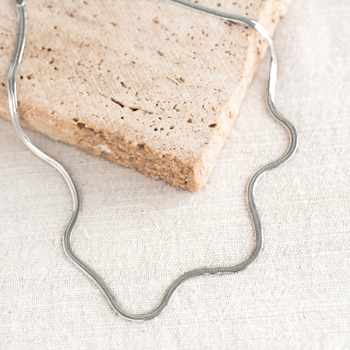 Snake Chain Necklace Silver with sleek flat design displayed on textured neutral fabric background