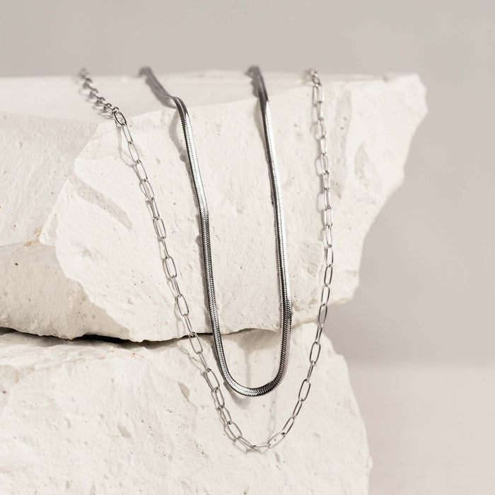Snake Chain Necklace Silver displayed draped over textured white stone with soft neutral background