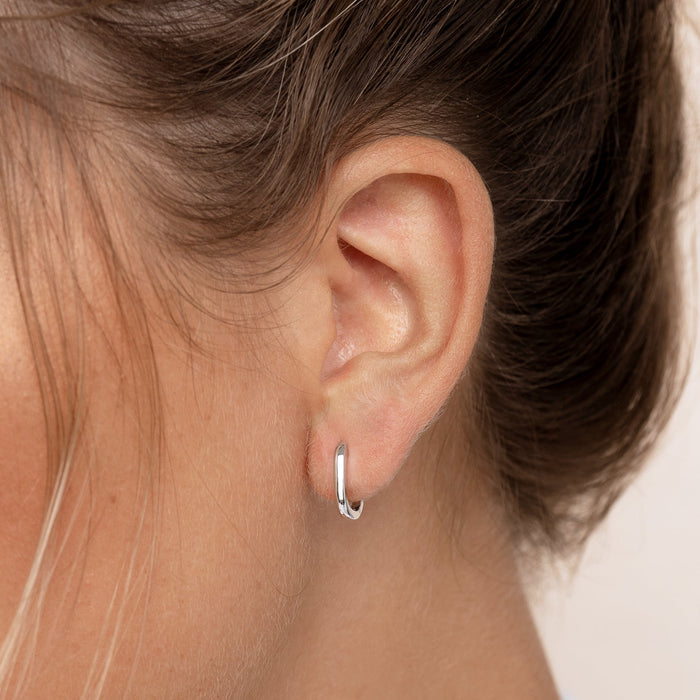 Close-up of a woman wearing Square Huggie Earrings Silver - Amelia with a neutral skin tone background