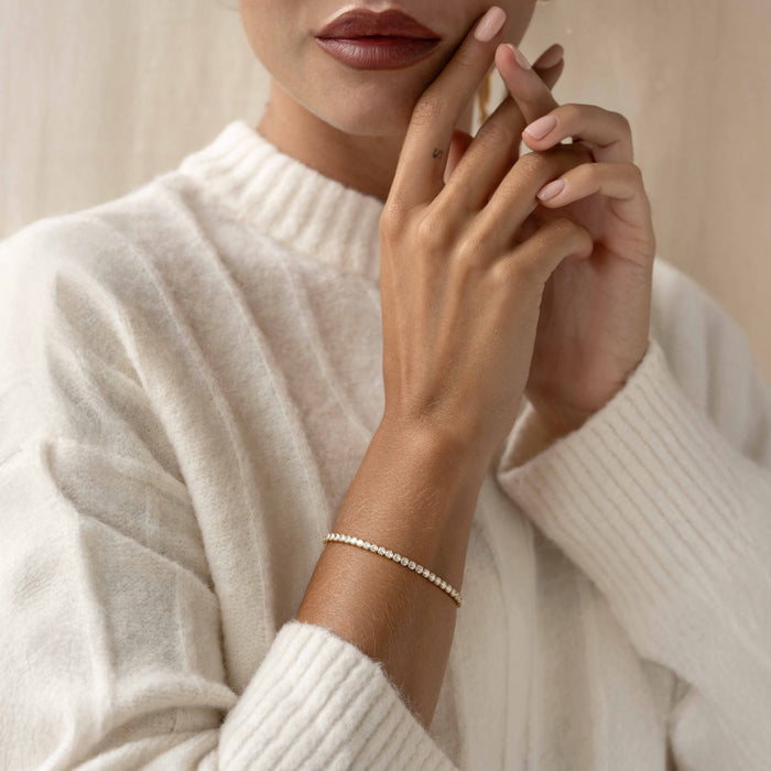Woman wearing a white sweater showcasing a delicate Tennis Bracelet - Zilla with round cubic zirconia stones in gold vermeil