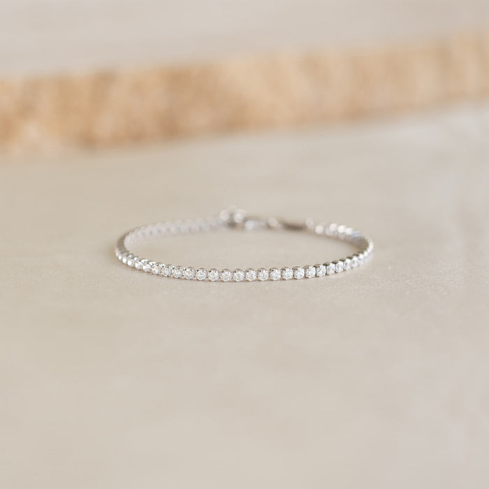 Close-up of Tennis Bracelet Silver - Audrey featuring sparkling cubic zirconia stones on a sterling silver chain resting on a beige surface