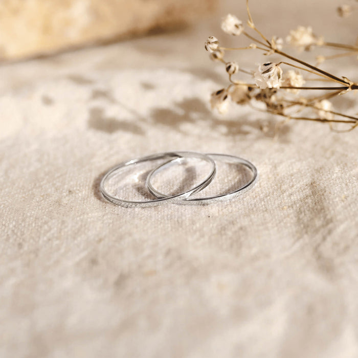 Two thin white gold rings on a textured beige fabric with delicate dried flowers, Thin White Gold Ring - Elin
