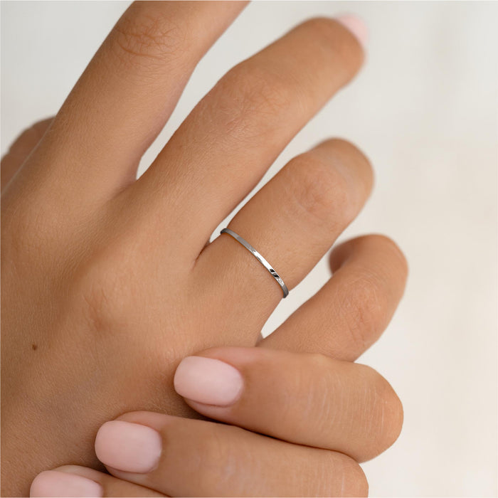 Close-up of a hand wearing the Thin White Gold Ring - Elin with a smooth, polished finish on a neutral background