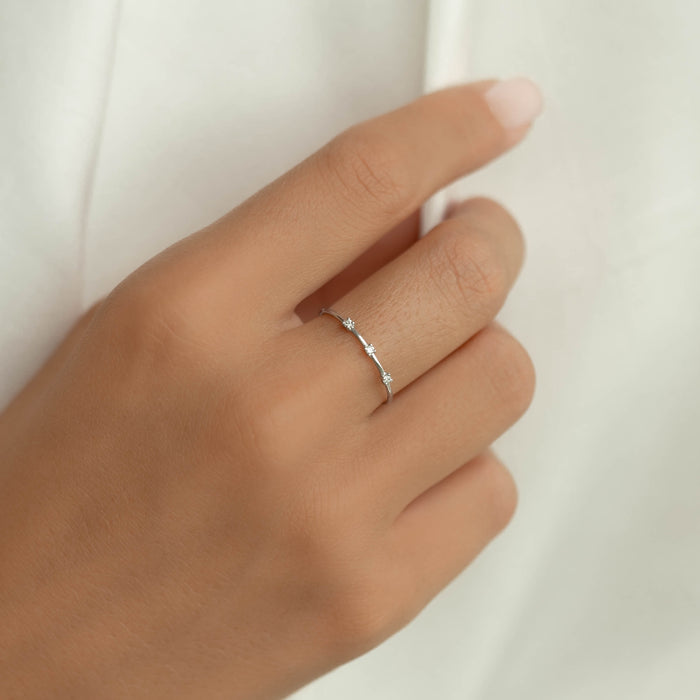 Close-up of a hand wearing the Three Stone Diamond Ring White Gold - Estelle on a neutral background