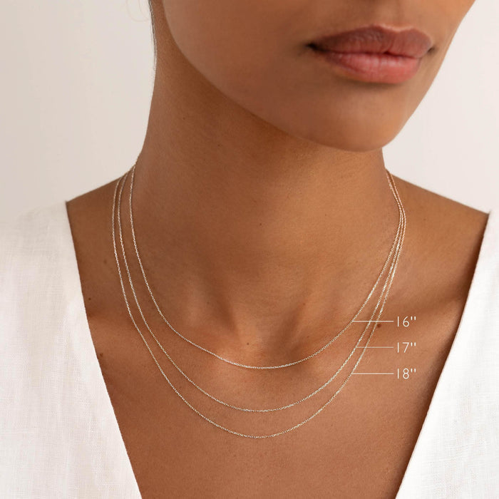 Close-up of a woman wearing the White Gold Cable Chain Necklace (16 inches) - Tyra layered with longer lengths on a neutral background