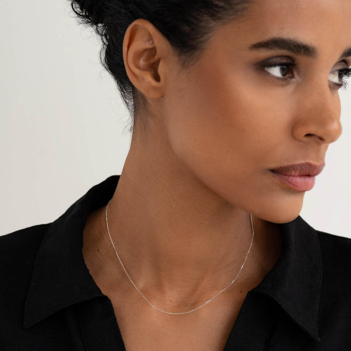 Close-up of a woman wearing the White Gold Cable Chain Necklace (16 inches) - Tyra with a black collared shirt on a light background