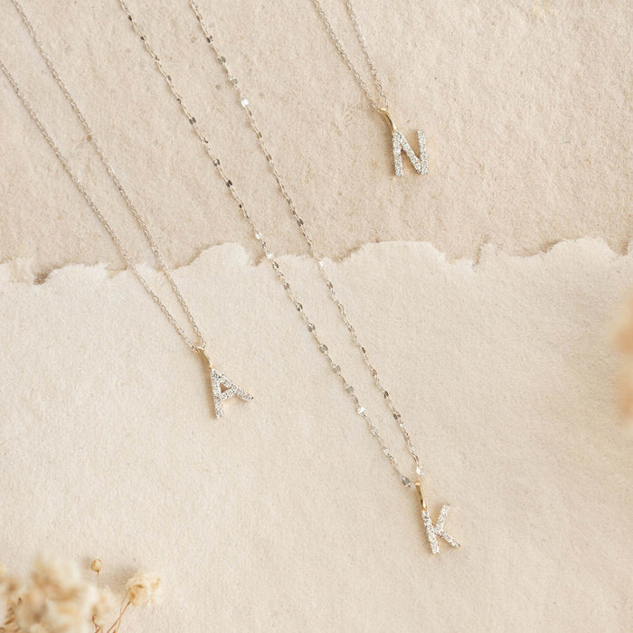 Three white gold initial charms A, N, and K on White Gold Cable Chain Necklace (16 inches) - Tyra on beige background