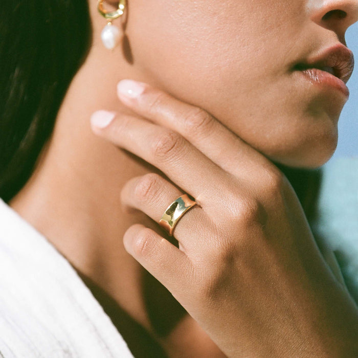 Close-up of a hand wearing the Wide Organic Ring - Essie in gold vermeil with soft natural light on a neutral background