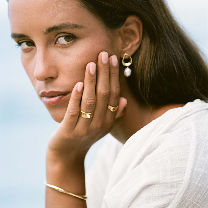 Close-up of a woman wearing the Wide Organic Ring - Essie and gold jewelry with neutral makeup and white top