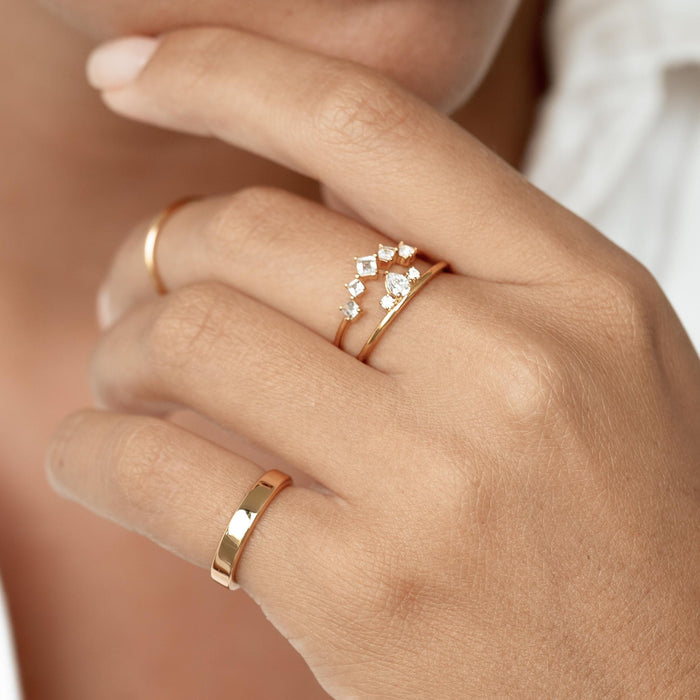 Close-up of hand wearing the Wide Ring - Paula gold band paired with a delicate gold ring on a neutral background